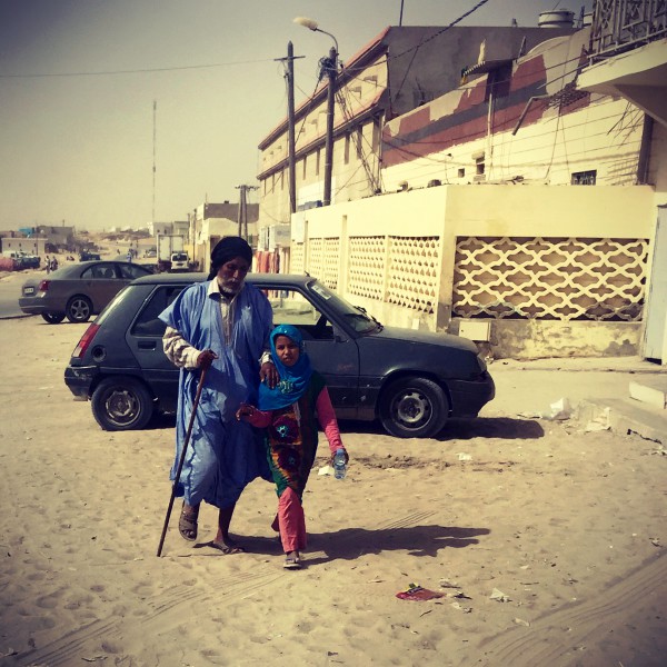 Un vieil homme avec une canne marche dans une rue ensablée de Nouadhibou en s'appuyant sur l'épaule d'une fillette #Off2Africa 14 Nouadhibou Mauritanie © Gilles Denizot 2016