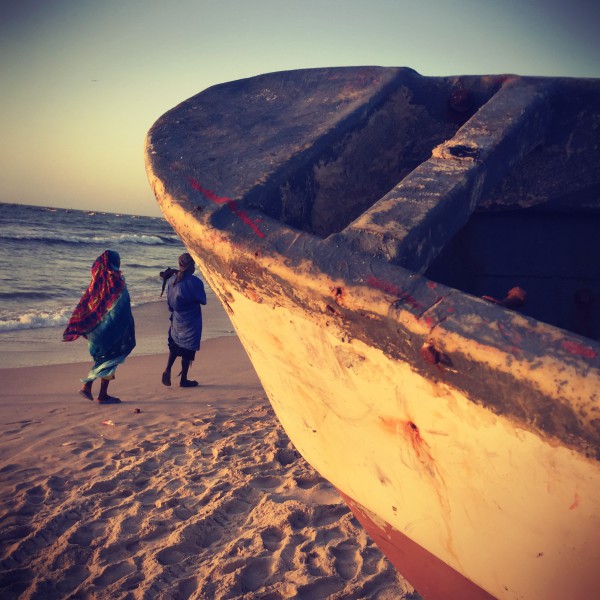 Deux silhouettes marchent sur le rivage à Nouakchott, une barque au premier plan #Off2Africa 17 Nouadhibou Nouakchott © Gilles Denizot 2016