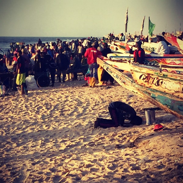 Un homme prie sur le sable devant une barque, au second plan la foule du marché aux poissons #Off2Africa 17 Nouadhibou Nouakchott © Gilles Denizot 2016