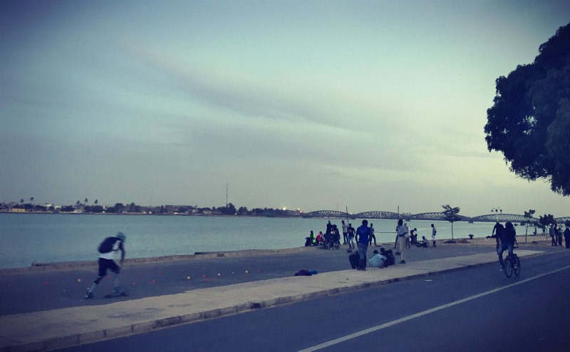 Le long du fleuve une foule de gens au crépuscule, certains assis en groupe, d'autres à vélo ou en planche à roulettes #Off2Africa 23 Saint-Louis Sénégal © Gilles Denizot 2016