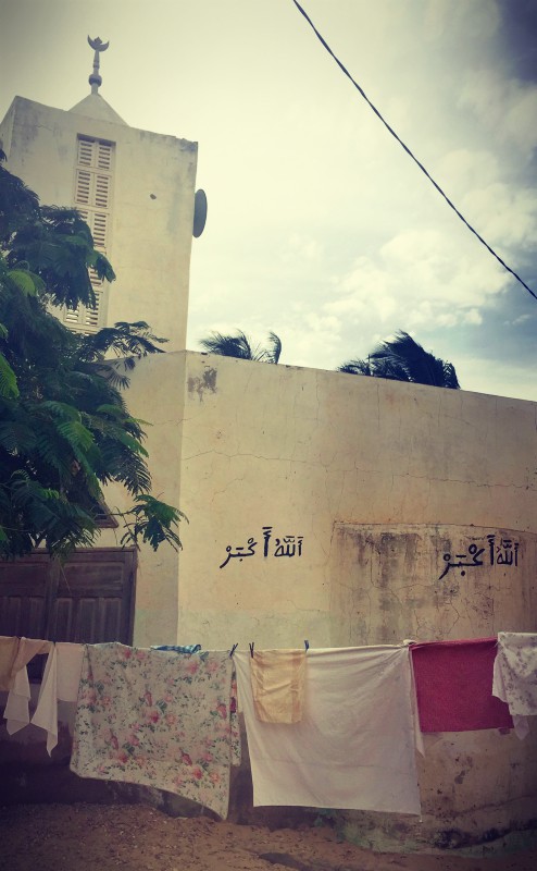 Une mosquée blanche et son minaret, des inscriptions en arabe sur le mur, devant il y a une corde et du linge qui sèche #Off2Africa 21 Saint-Louis Sénégal © Gilles Denizot 2016