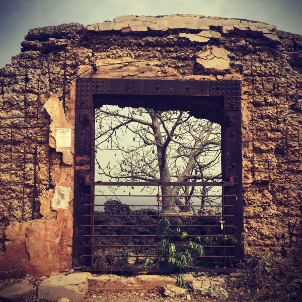 Dans un mur détruit, le cadre d'une porte en métal rouillé. À travers on voit un arbre. #Off2Africa 29 Gorée Sénégal © Gilles Denizot 2016