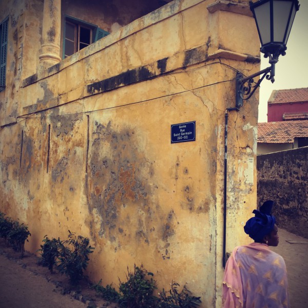 Mur et bâtisse jaune décrépis et une femme vêtue de rose et bleu #Off2Africa 29 Gorée Sénégal © Gilles Denizot 2016