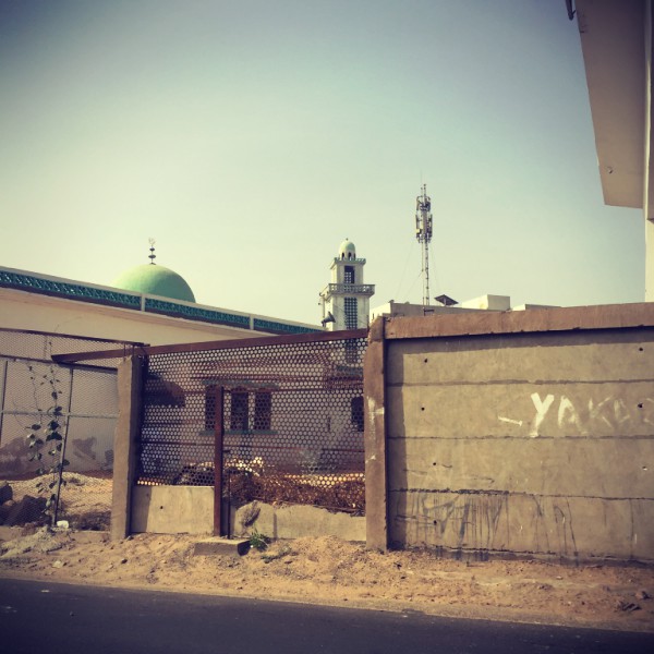 On distingue une mosquée et son minaret derrière des murs en bord de route #Off2Africa 35 Dakar Sénégal © Gilles Denizot 2016