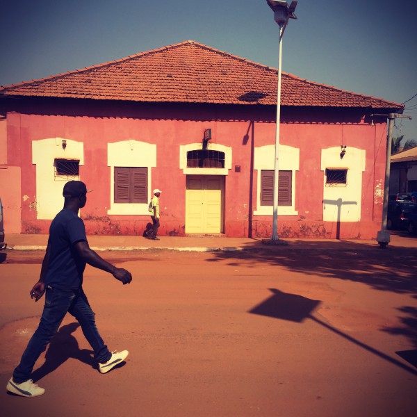 Maison ocre rose et deux hommes marchant devant #Off2África 49 Ziguinchor Bissau © Gilles Denizot 2017