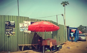 Dans une rue ensablée, un stand sous un parasol rouge #Off2Africa 69 Conakry Guinée © Gilles Denizot 2017