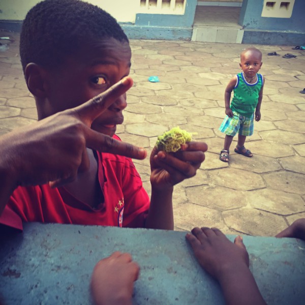 Un enfant dans une cour et au premier plan un garçon vêtu de rouge #Off2Africa 71 Conakry Guinée © Gilles Denizot 2017