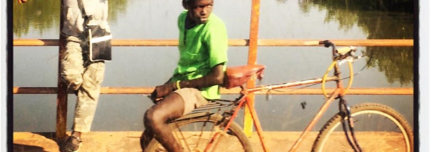 Un garçon chemise verte sur l'arrière d'un vélo, un autre sweat-shirt blanc accoudé sur la rambarde d'un pont #Off2África 49 Ziguinchor Bissau © Gilles Denizot 2017