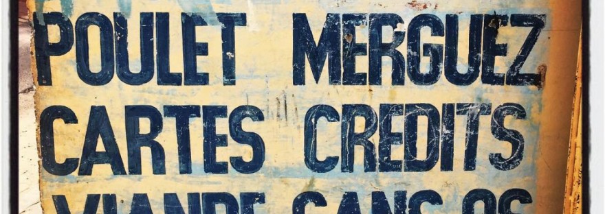 Sur un mur jaune décrépi, il est écrit : saucisson nems poulet mergues cartes credits viande sans os foie #Off2Africa 21 Saint-Louis Sénégal © Gilles Denizot 2016