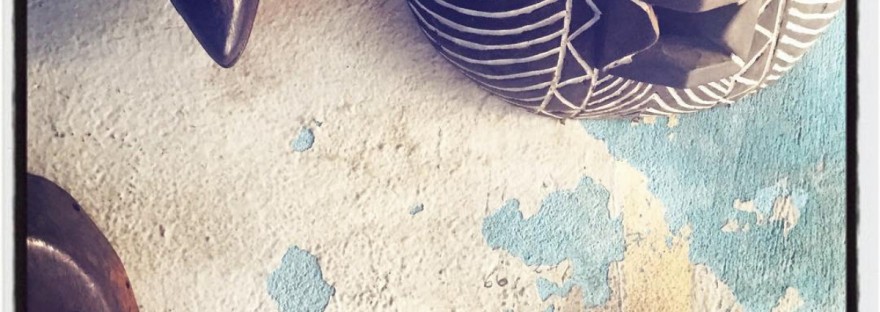 Trois masques africains en bois sont accrochés sur un mur décrépi bleu ciel et blanc, on y voit aussi quelques inscriptions au feutre noir #Off2Africa 77 Conakry Guinée © Gilles Denizot 2017