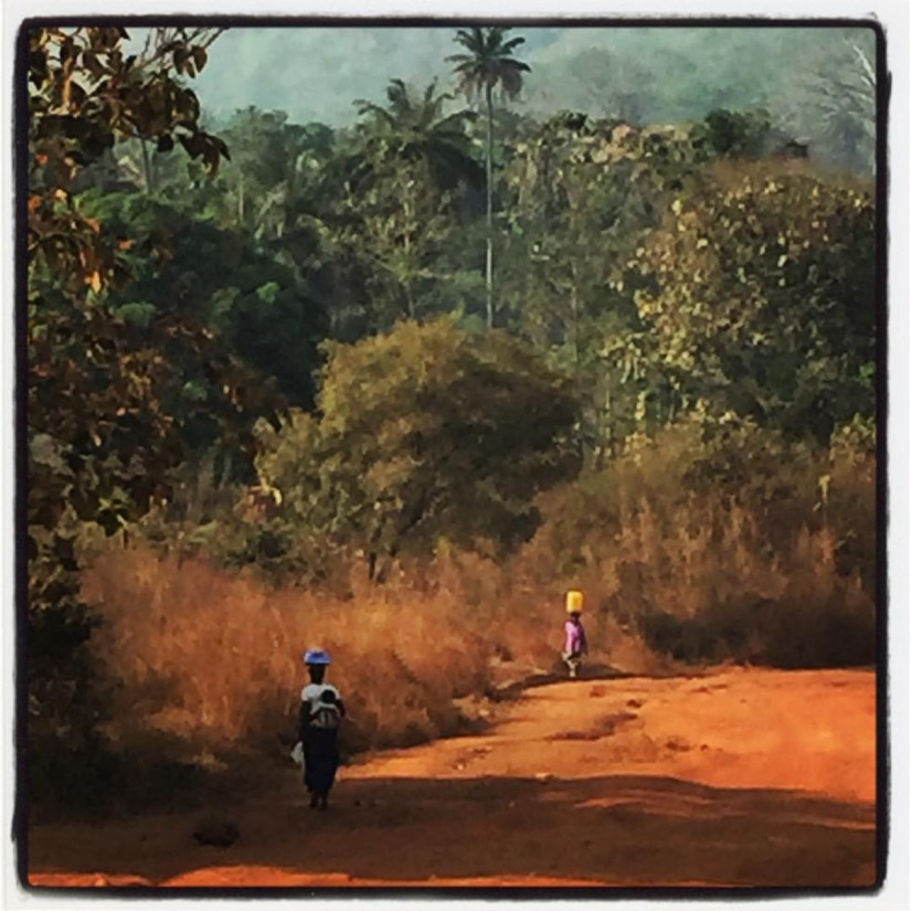 En Guinée, une route en terre rouge, des arbres à perte de vue et deux femmes marchant, des récipients sur la tête #Off2Africa 61 Kindia Guinée © Gilles Denizot 2017
