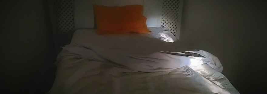 Un rayo de luz cae sobre una cama toda blanca, con almohada naranja #InAfrica Carcajada © Gilles Denizot 2017