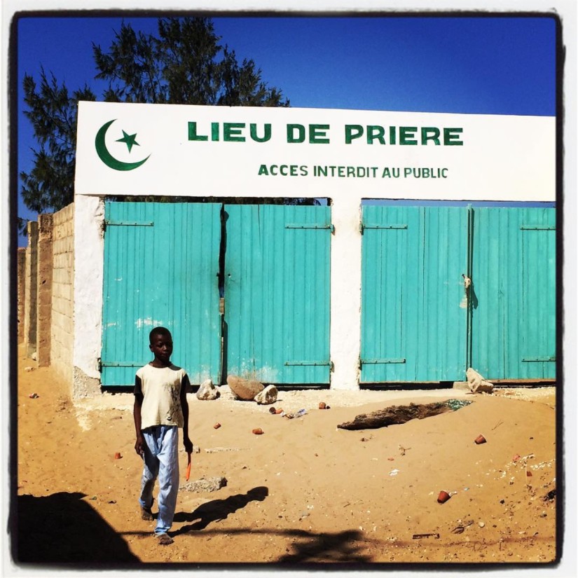 Un garçon pieds nus, vêtu d'un jeans et d'un t-shirt marche devant un lieu de prière musulman, accès interdit au public #Off2Africa 42 Dakar Sénégal © Gilles Denizot 2017
