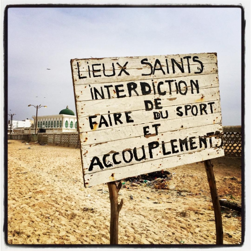 Un panneau sur la plage de Yoff informe : Lieux saints, Interdiction de faire du sport et accouplements. Derrière le panneau, une mosquée. #Off2Africa 28 Dakar Sénégal © Gilles Denizot 2016