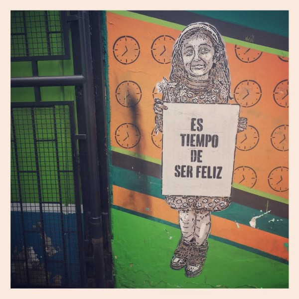 Peinture murale à Bogotá représentant une fille tenant un panneau. On y lit : Es tiempo de ser feliz