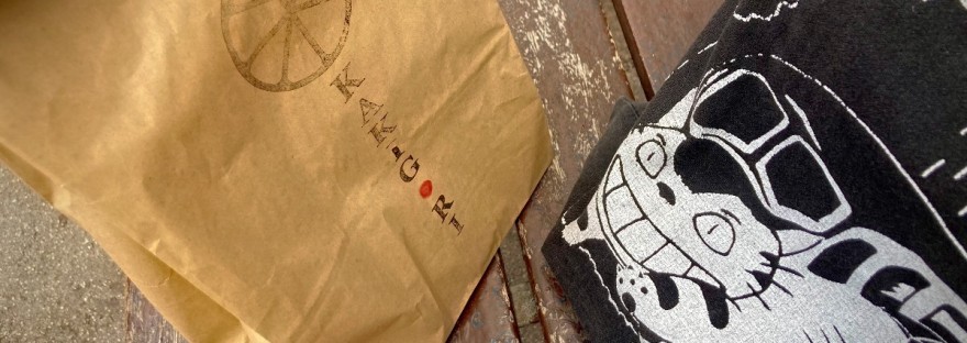 Sachet en papier kraft de Kakigori posé sur un banc à côté d'un sac illustré manga ©GD24 #HolaBCN Gouttes de grâce