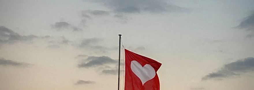 Sur fond de ciel crépusculaire, un lointain cousin du drapeau suisse, mais la croix blanche a été remplacée par un cœur blanc #Off2Europe Genève ©GD23
